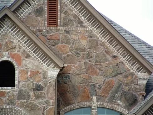 Stone and brick house exterior with arched window and decorative trim.