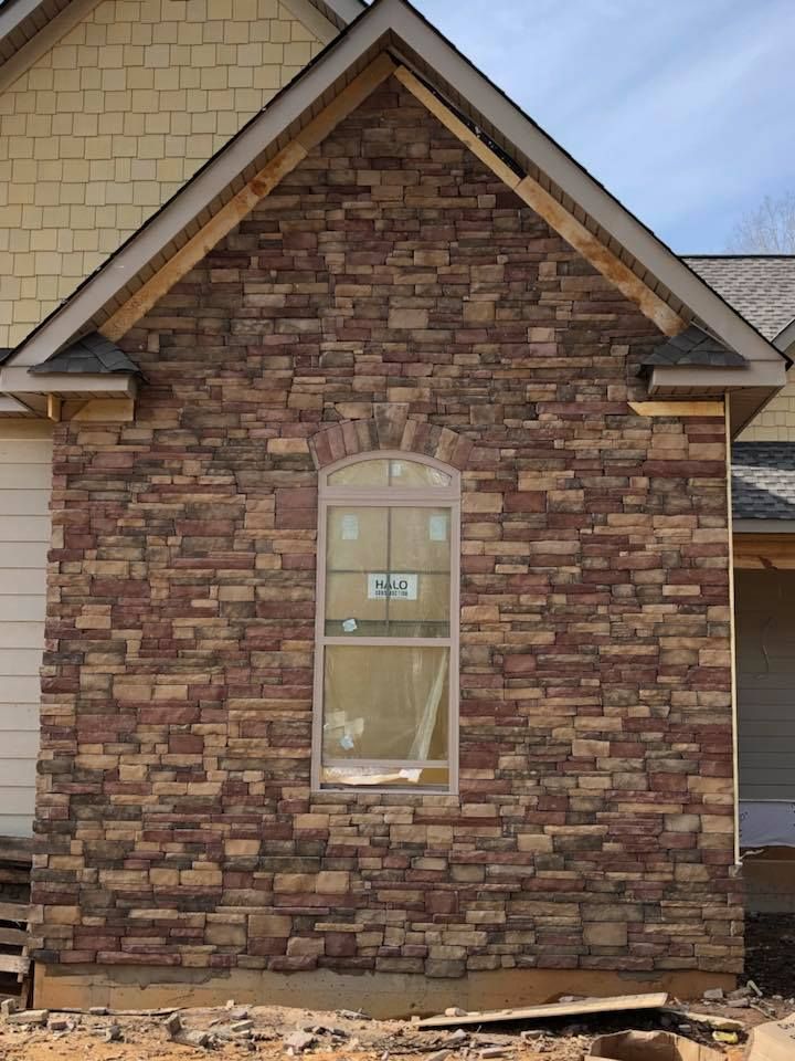 Stone exterior of a house with an arched window; unfinished construction with wood framing.