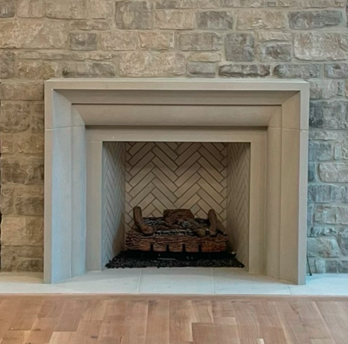 Fireplace with stone surround and herringbone brick interior, set against a stone wall.