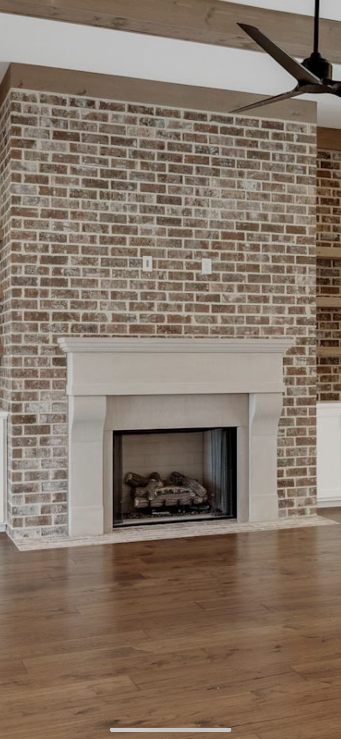 Brick fireplace with a stone mantel in a room with hardwood floors. Ceiling fan.