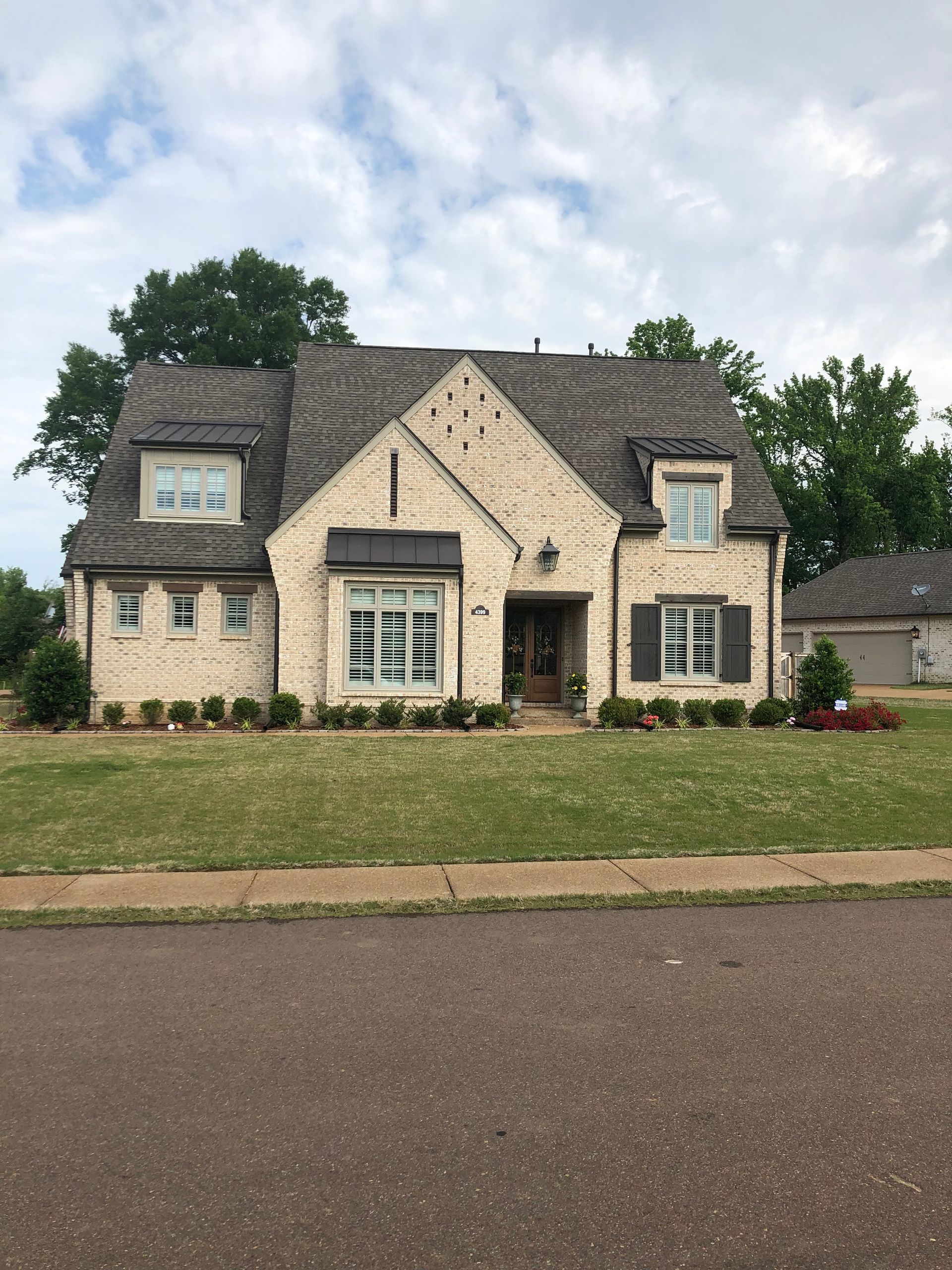 Beige brick house with gray roof and shutters, a small front yard, and a cloudy sky.