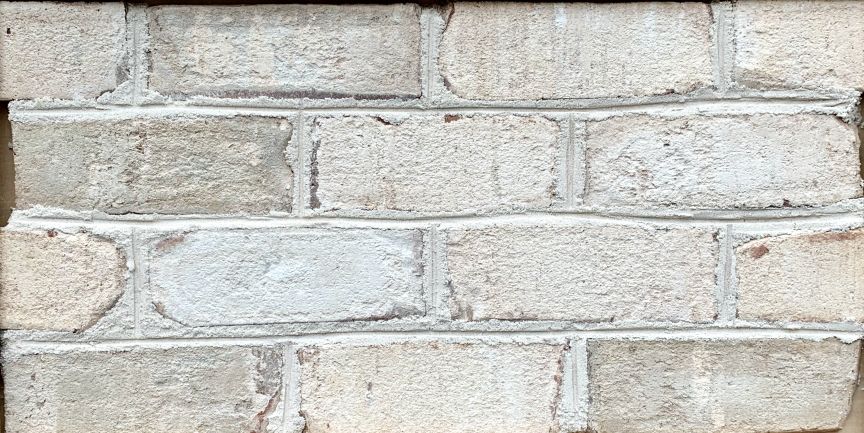 Close-up of a weathered brick wall. The bricks are pale, with dark mortar between them.