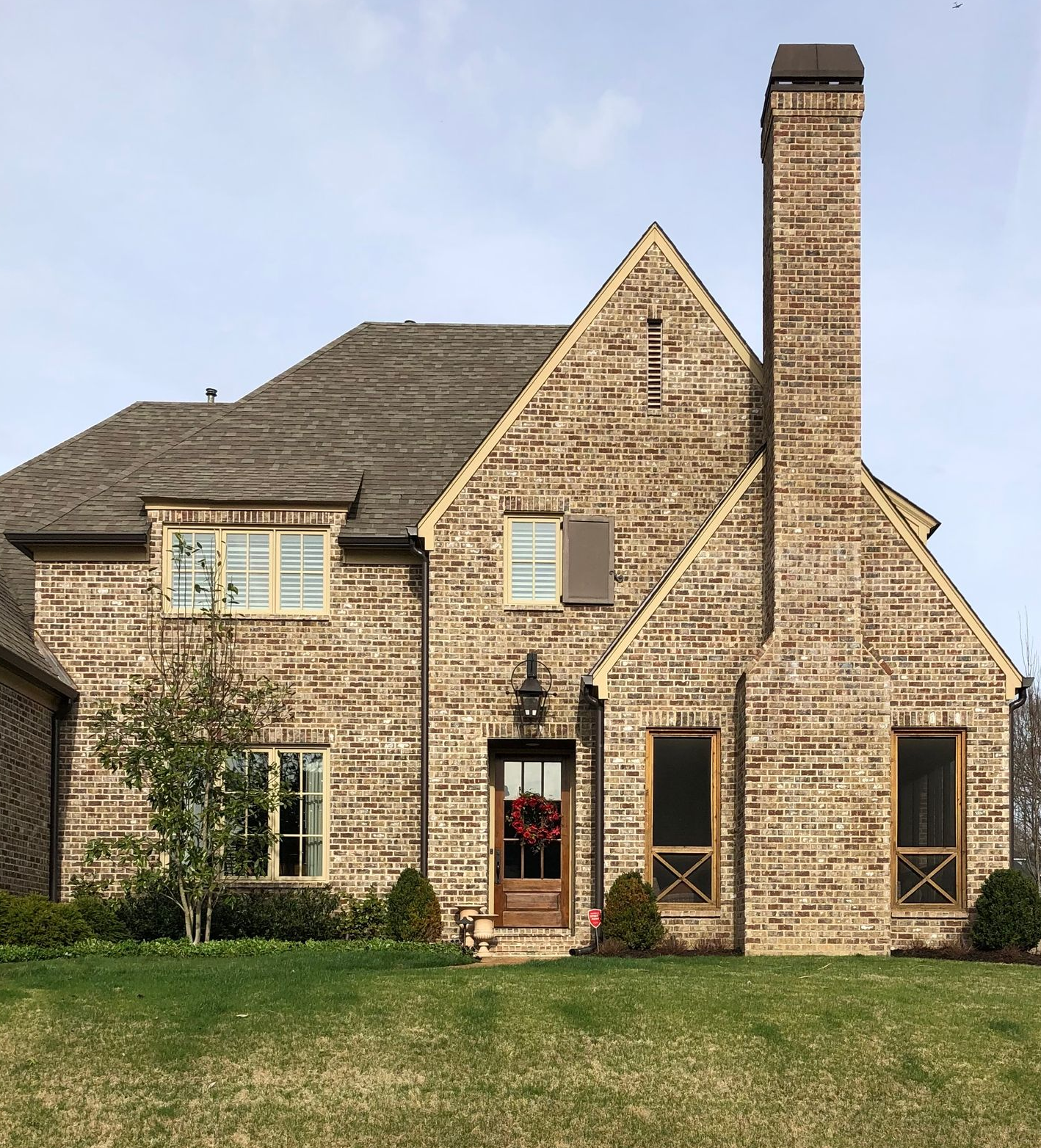 Brick two-story house with a prominent chimney, brown roof, and front door with a wreath.