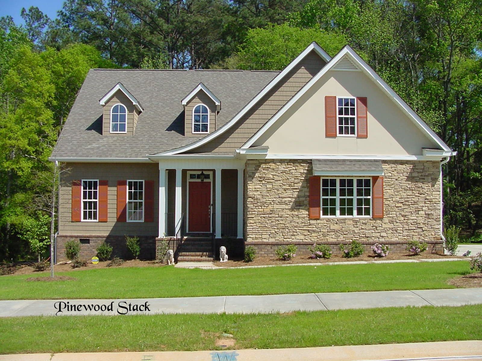 Tan and stone-faced house with red door, shutters, and dormers on a green lawn.