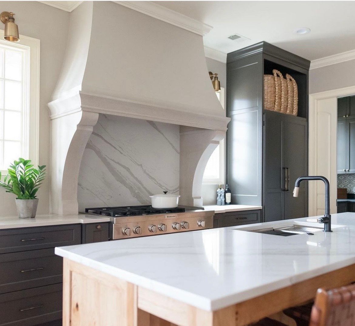 Elegant kitchen with marble countertops, dark cabinets, range hood, and island.