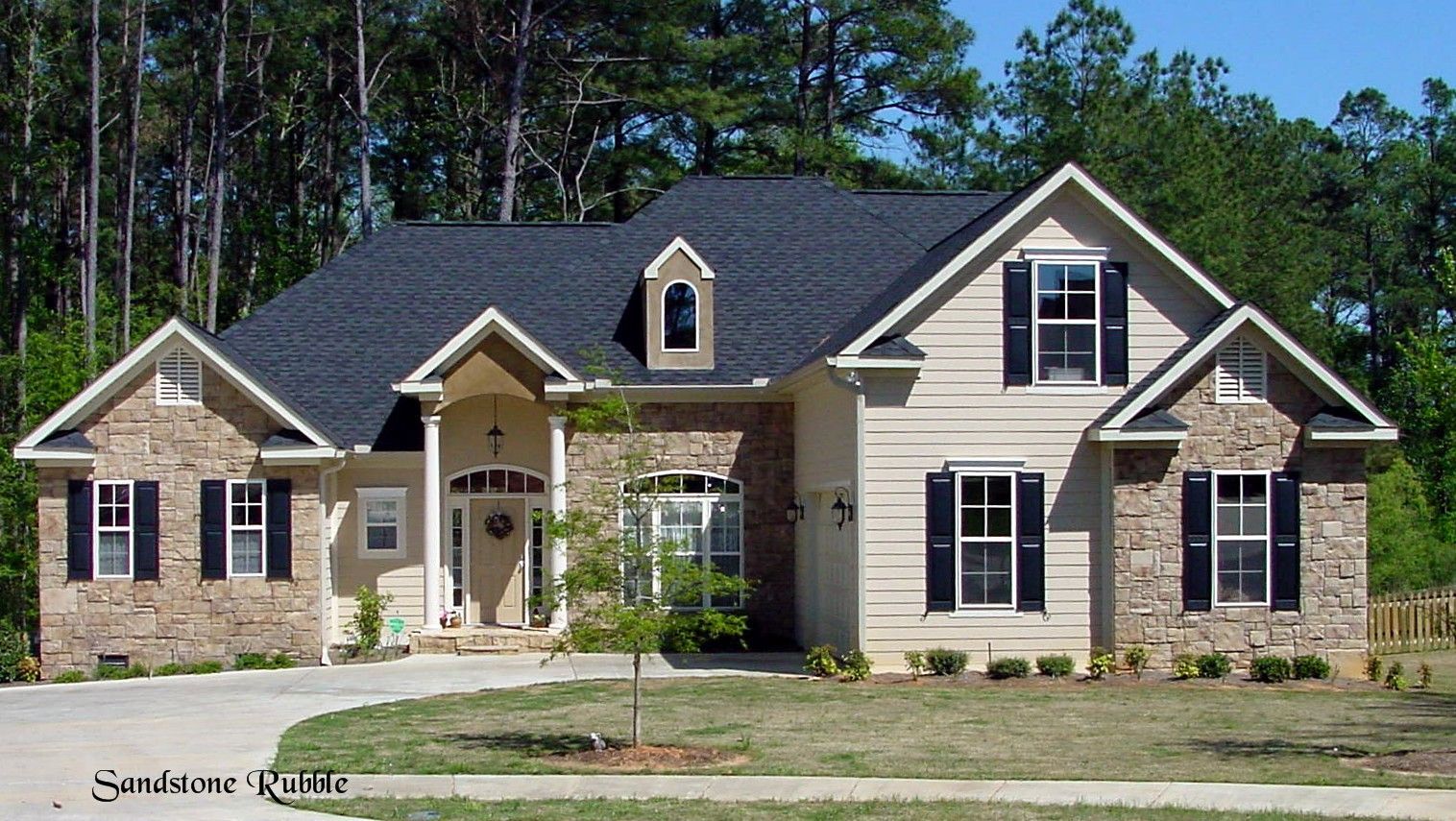 Two-story house with beige siding, brick accents, black shutters, and a dark roof.