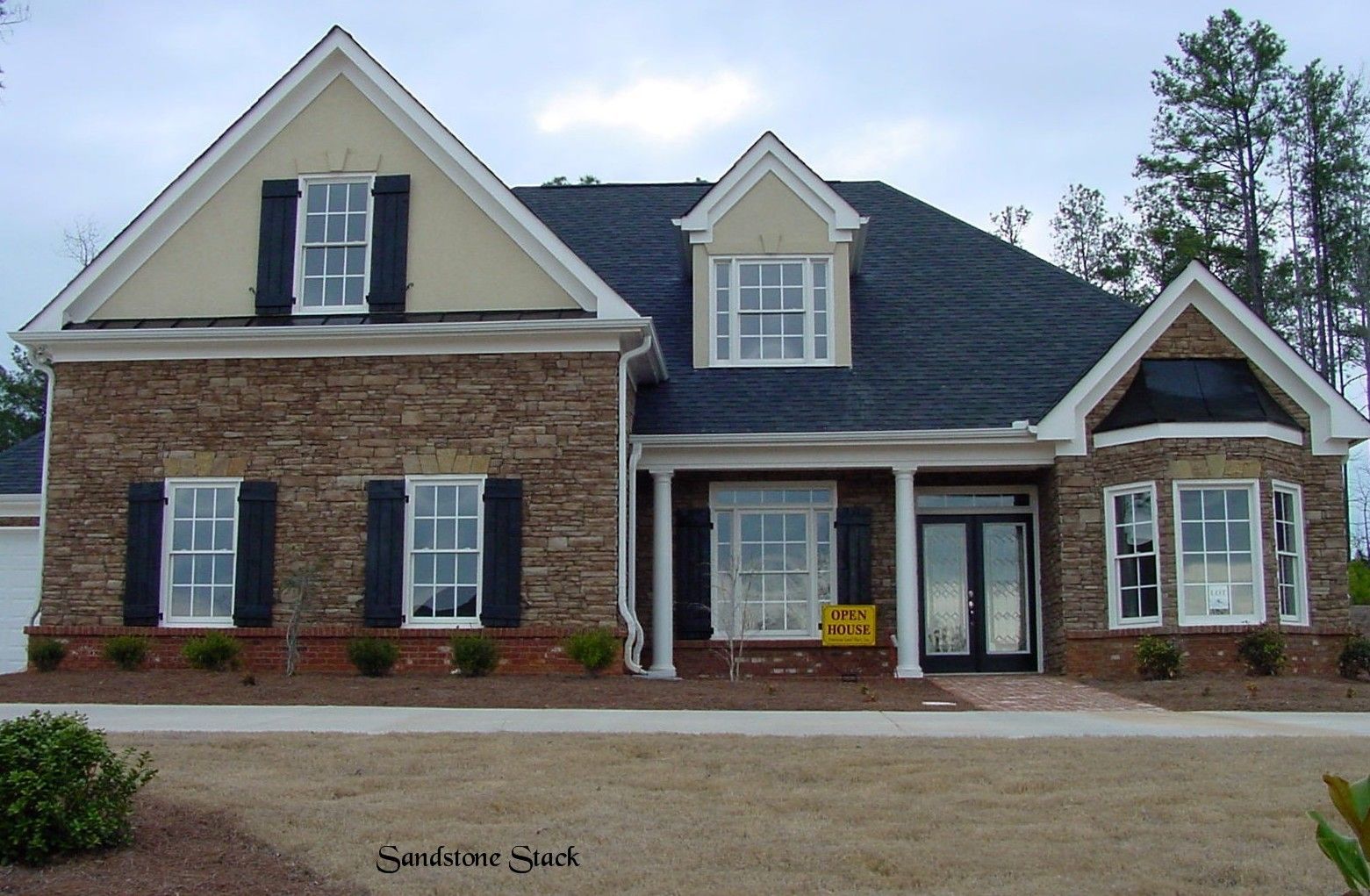 Tan and brown stone house with black shutters, brick walkway, and dark roof.