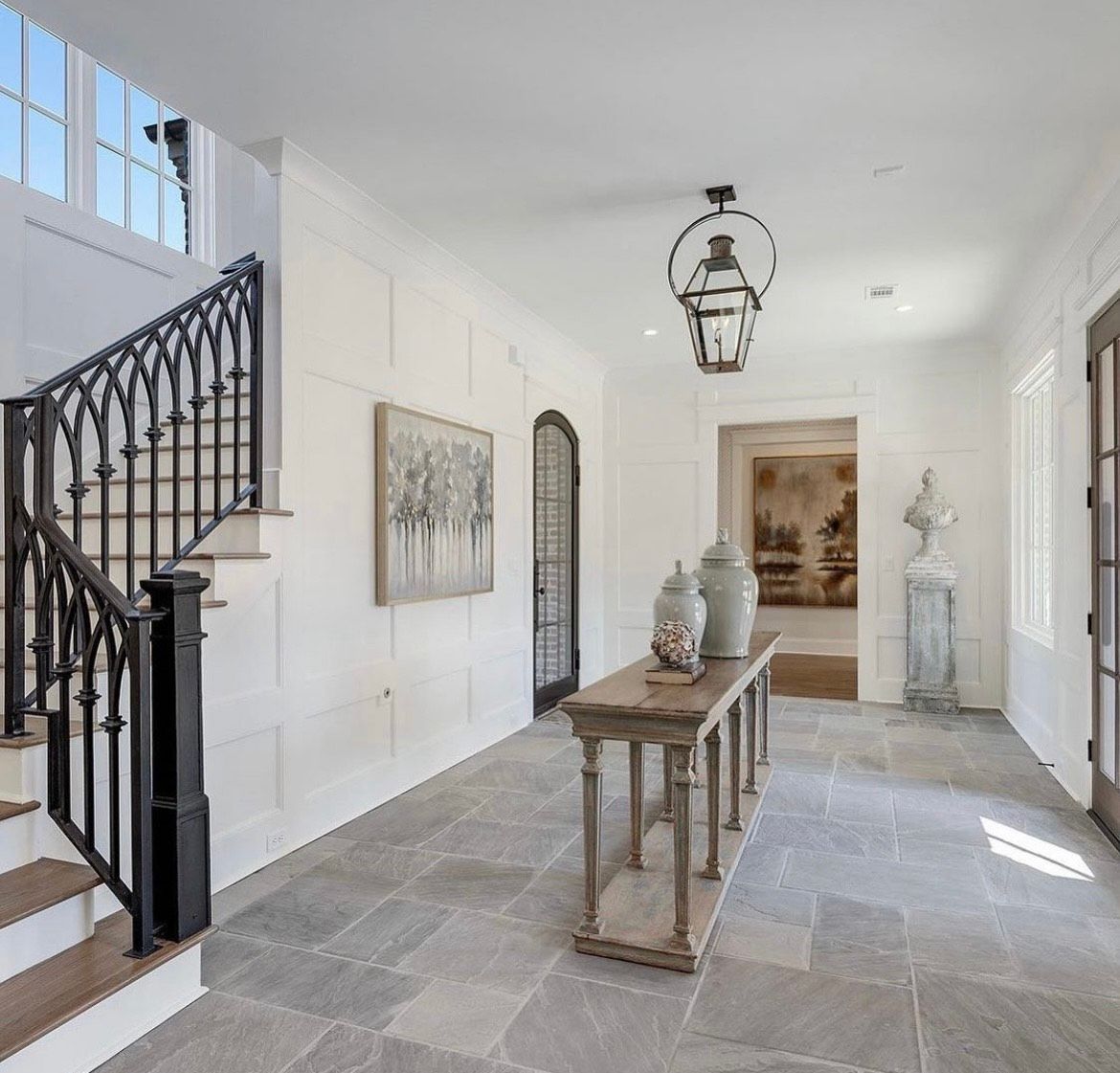 Hallway with stone floor, staircase, console table, artwork, and arched doorway.