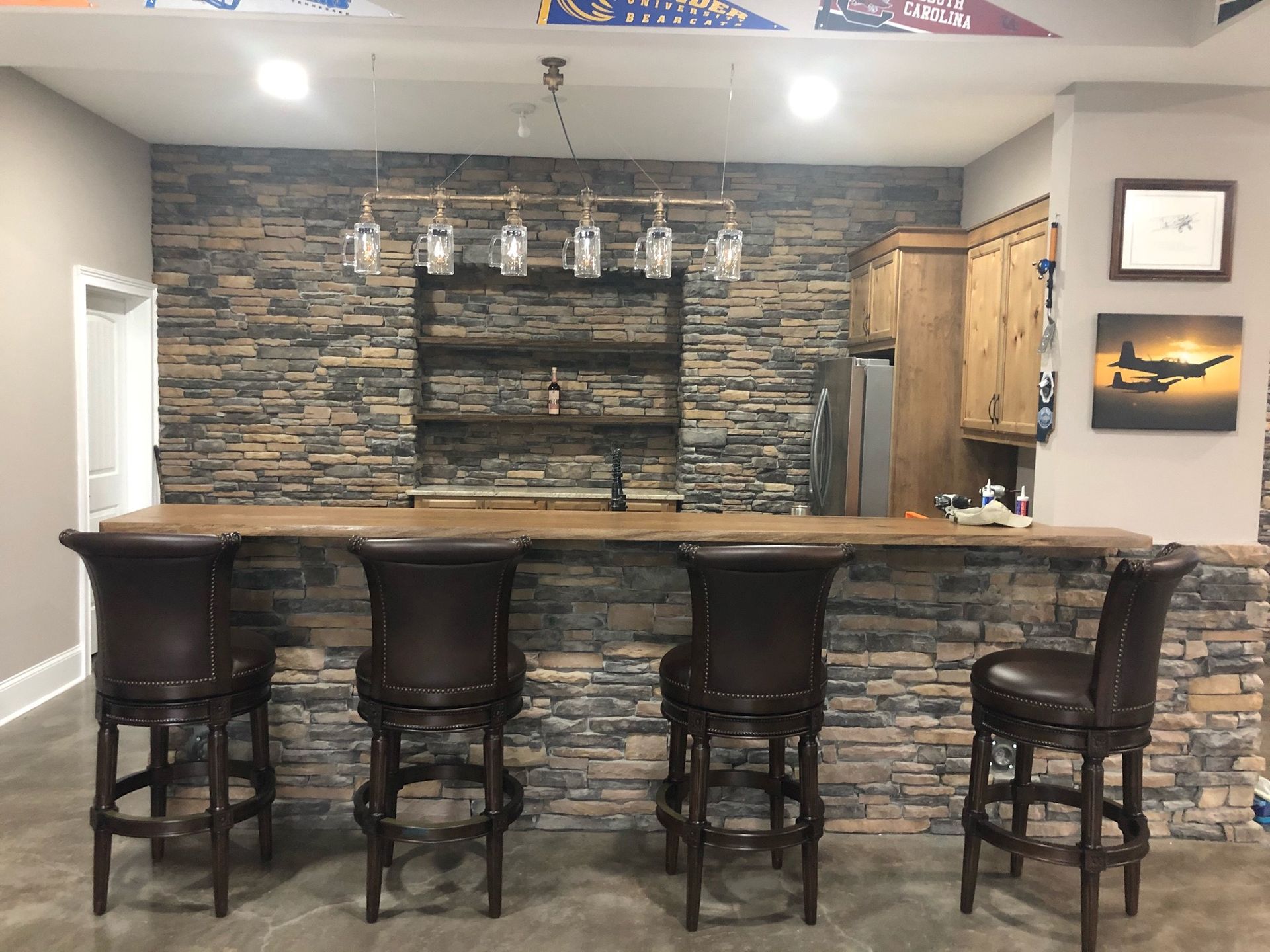 Basement bar with stone facade, wooden countertop, bar stools, and liquor display.