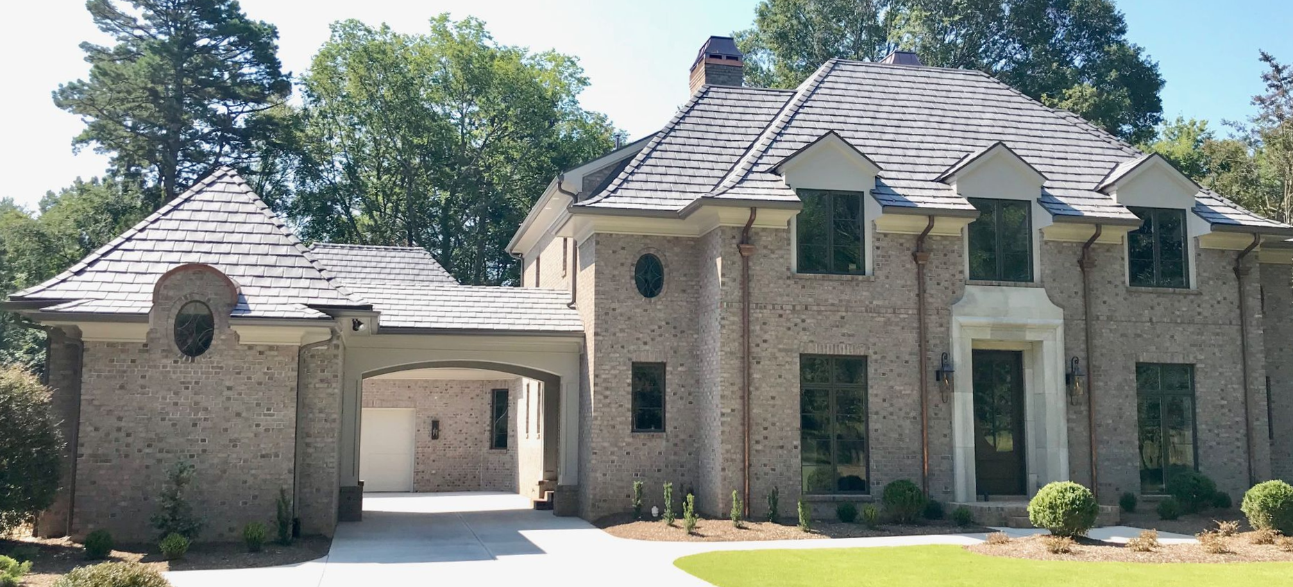 Brick house with arched driveway, gray roof, and green lawn.