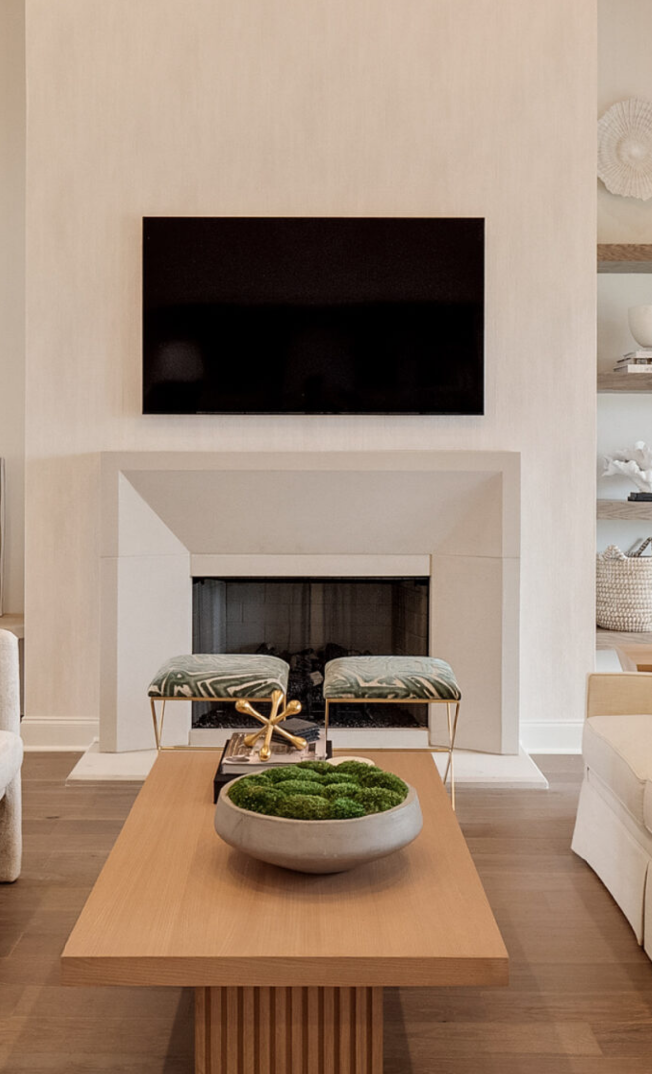 Living room with fireplace, TV above. Light-colored walls, wood floor, modern furniture, and a coffee table.