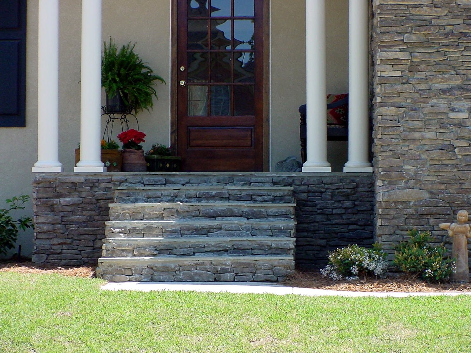 Stone steps leading to a front porch with columns and a dark wooden door.