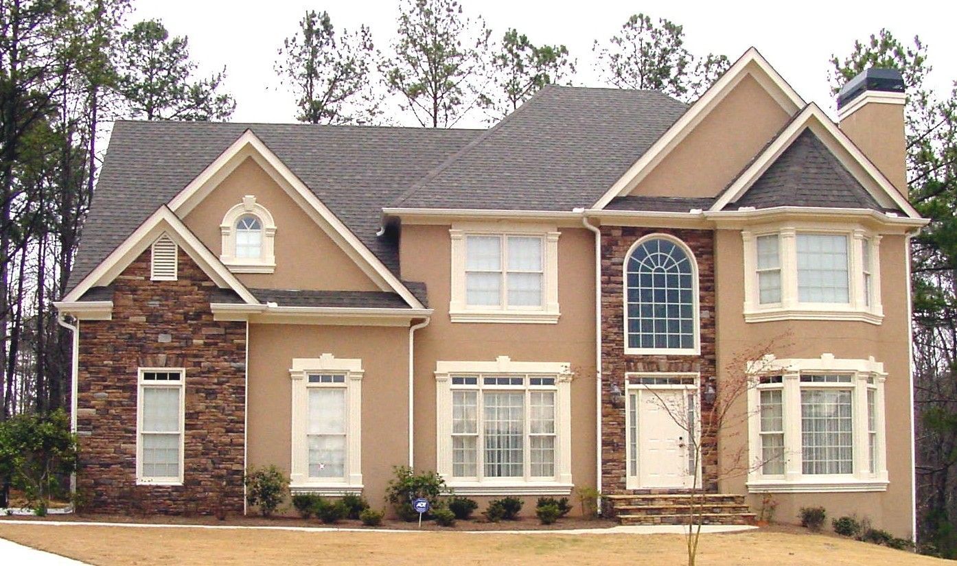 Two-story tan house with a stone accent and a dark roof.