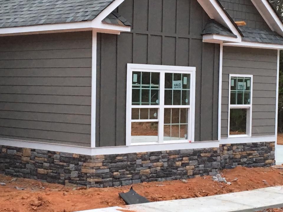 House exterior with gray siding, stone base, white window frames, and brown roof.