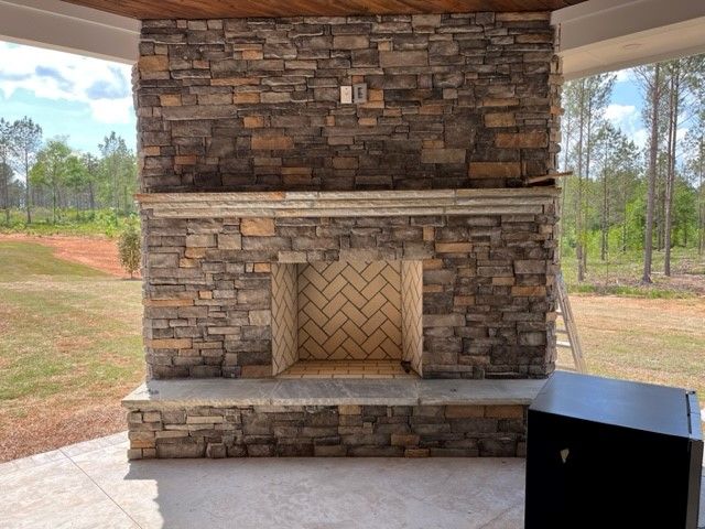 Stone fireplace with brick firebox, on a patio, under a covered area, surrounded by nature.