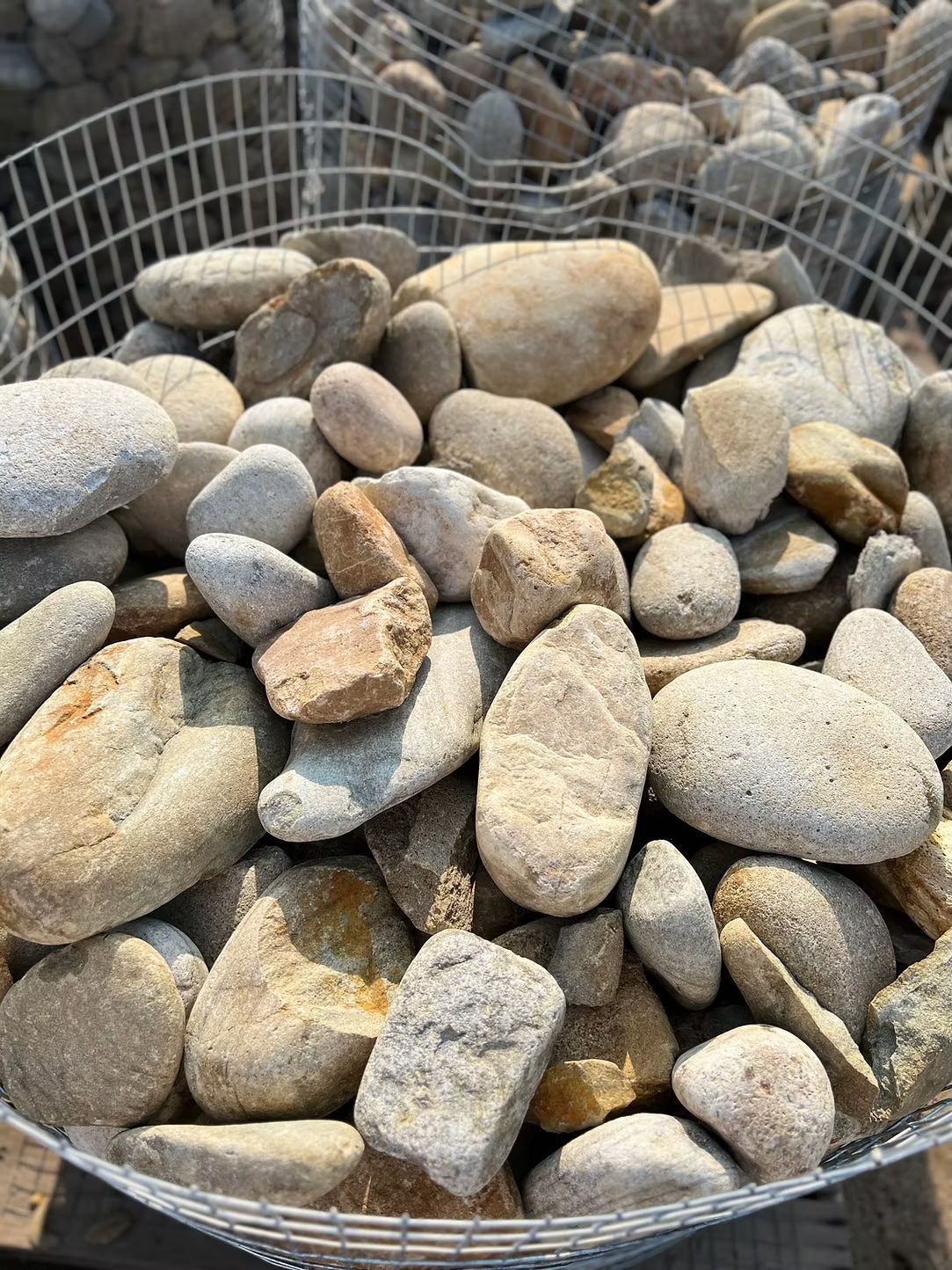 Pile of smooth, beige and tan river rocks in a wire basket.