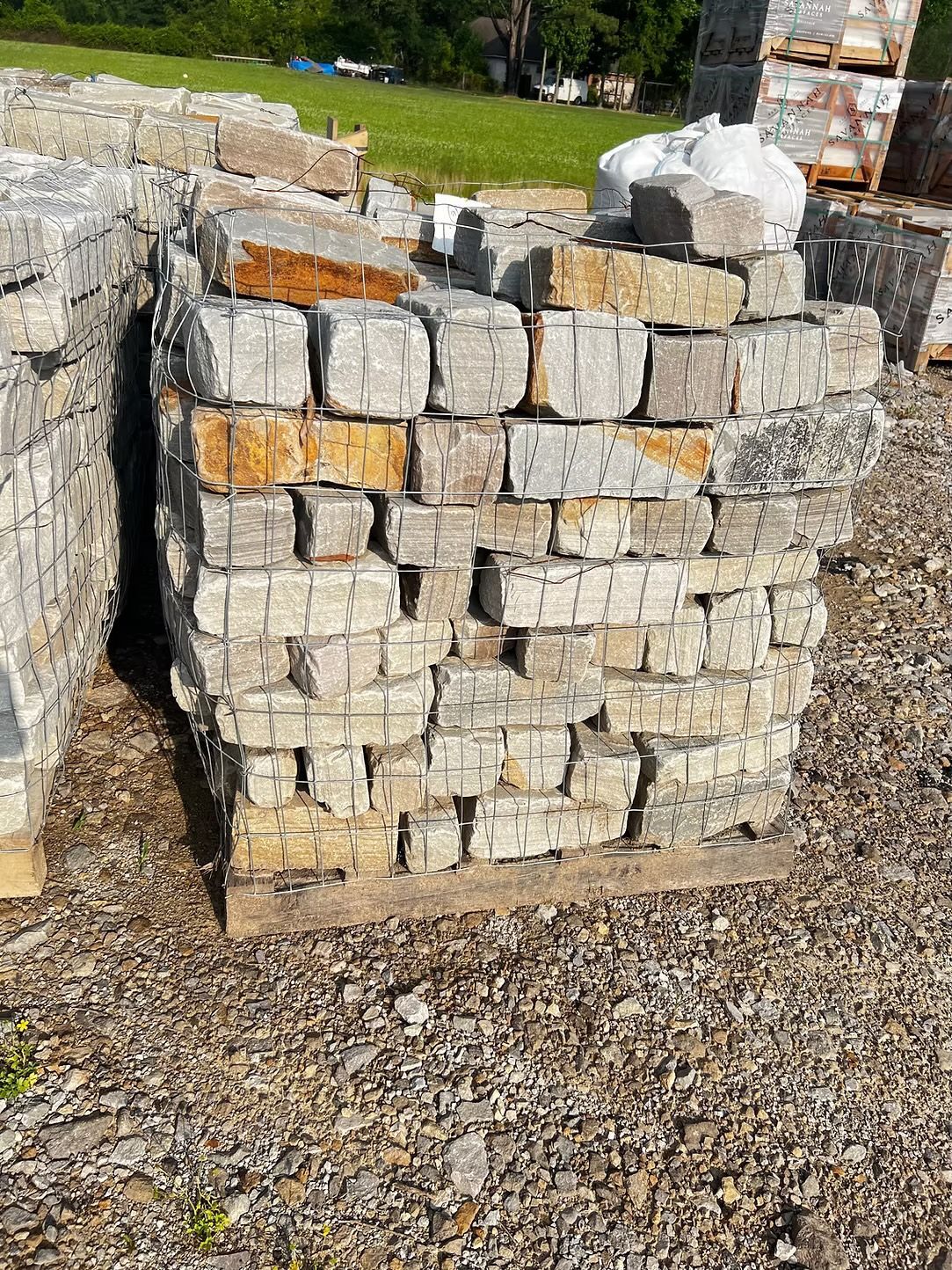 Pallet of stacked, square-cut stones, held together by metal wire. Some stones have orange-brown coloring. Gravel ground.