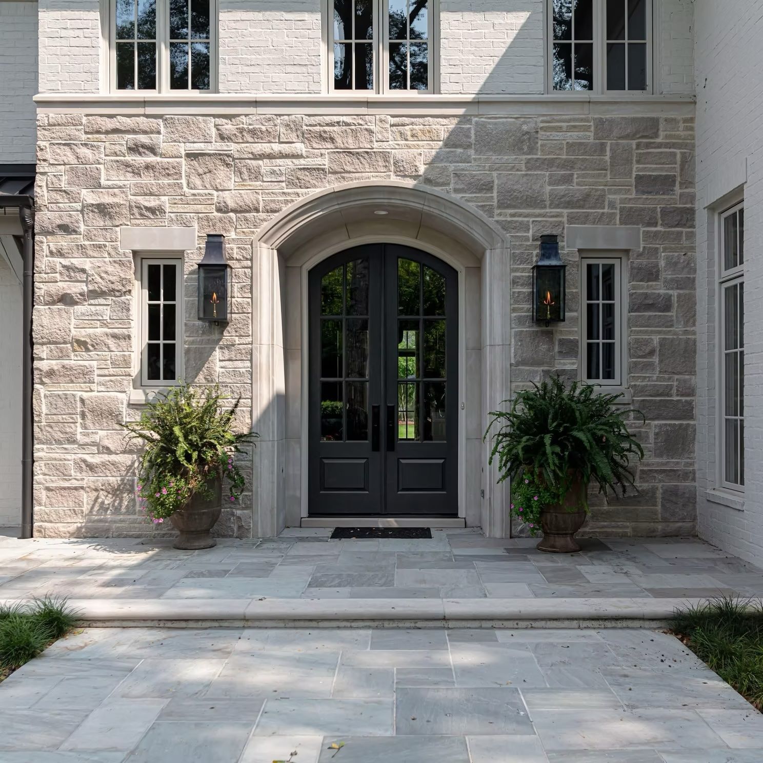 Stone facade entrance with arched black double doors, ferns in pots, and matching side windows.