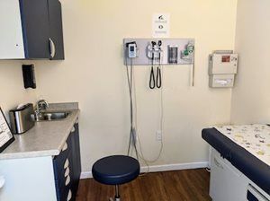 Doctor's office exam room with examination table, sink, medical tools, cabinets, and a stool.