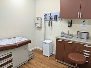 Examination room with a medical bed, sink, cabinets, and medical equipment.