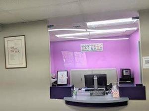 Reception desk with a protective barrier and computer, against a lavender-painted wall.