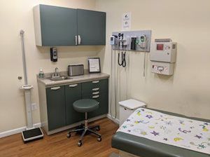 Examination room with cabinets, sink, exam table, and medical equipment.