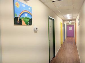 Hallway with colorful doors, artwork, and wooden floor.