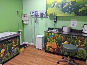 Pediatric exam room with jungle-themed cabinets, medical equipment, and green walls.