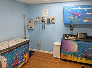 Pediatric examination room with blue walls, ocean-themed cabinets, a changing table, and medical equipment.