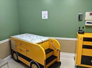 Yellow school bus-shaped examination bed in a medical room with green walls and yellow cabinet.