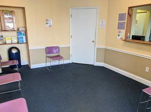 Empty waiting room with purple chairs, a closed door, and informational posters on walls.