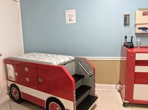 Red fire truck-shaped pediatric examination table with steps in a doctor's office.