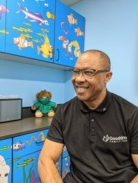 Man in glasses smiles, sits in a room with blue cabinets decorated with underwater drawings.