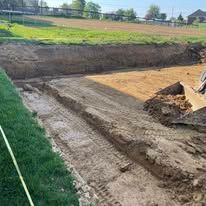 Backyard excavation site with a dirt pit, graded soil, and a green lawn in the foreground