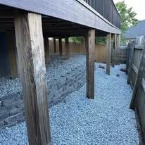Raised wooden deck over gravel path with weathered posts and brick wall underneath