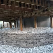Low stone retaining wall beneath a raised wooden deck over gravel ground