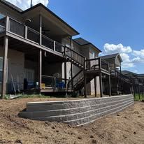 Row of elevated apartment units with stairs and a terraced retaining wall under a blue sky