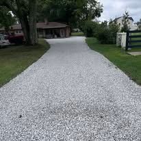 Gravel driveway leading to a house with trees and lawn on both sides