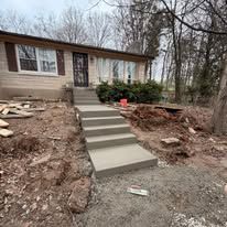 Front steps leading to a house, with fresh concrete walkway and sloped dirt landscaping.