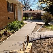 Residential sidewalk beside a brick house, leading past a curved walkway under construction.