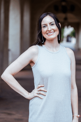 A woman in a white dress is standing with her hand on her hip and smiling.