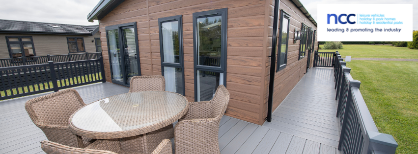 a brown clad caravan with grey decking area with table and chairs
