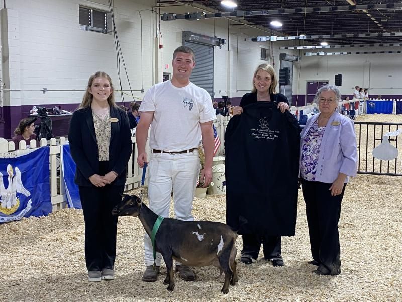 Four people standing with a goat at a livestock show in an indoor arena