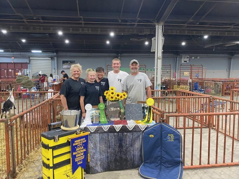 Five people posing behind a decorated booth with sunflowers at an indoor livestock event