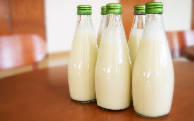 Four glass bottles of creamy white liquid with green caps on a wooden table.