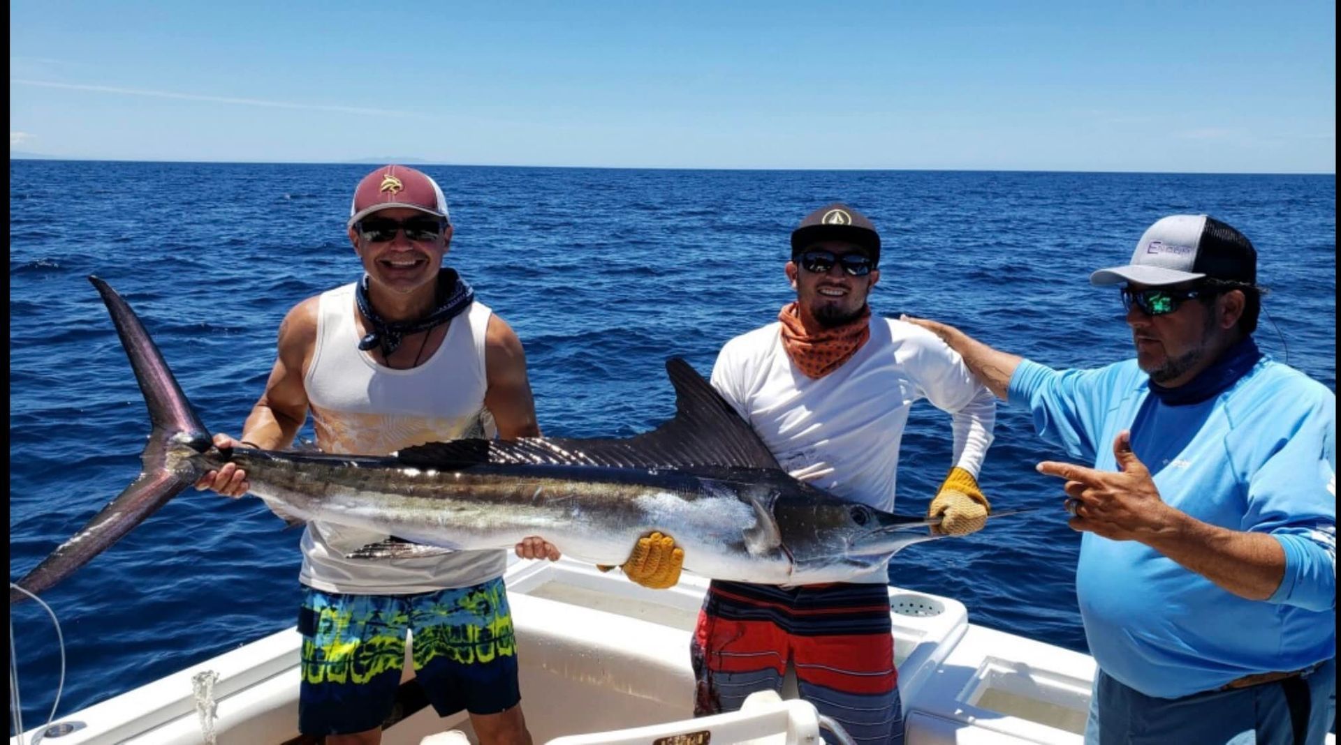Three men are standing on a boat holding a large fish.