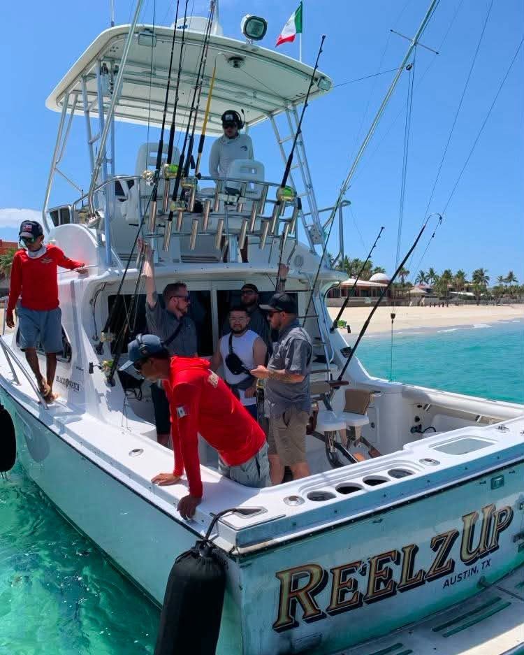 Fishing boat docked by a beach under a clear blue sky, with anglers on the pier.
