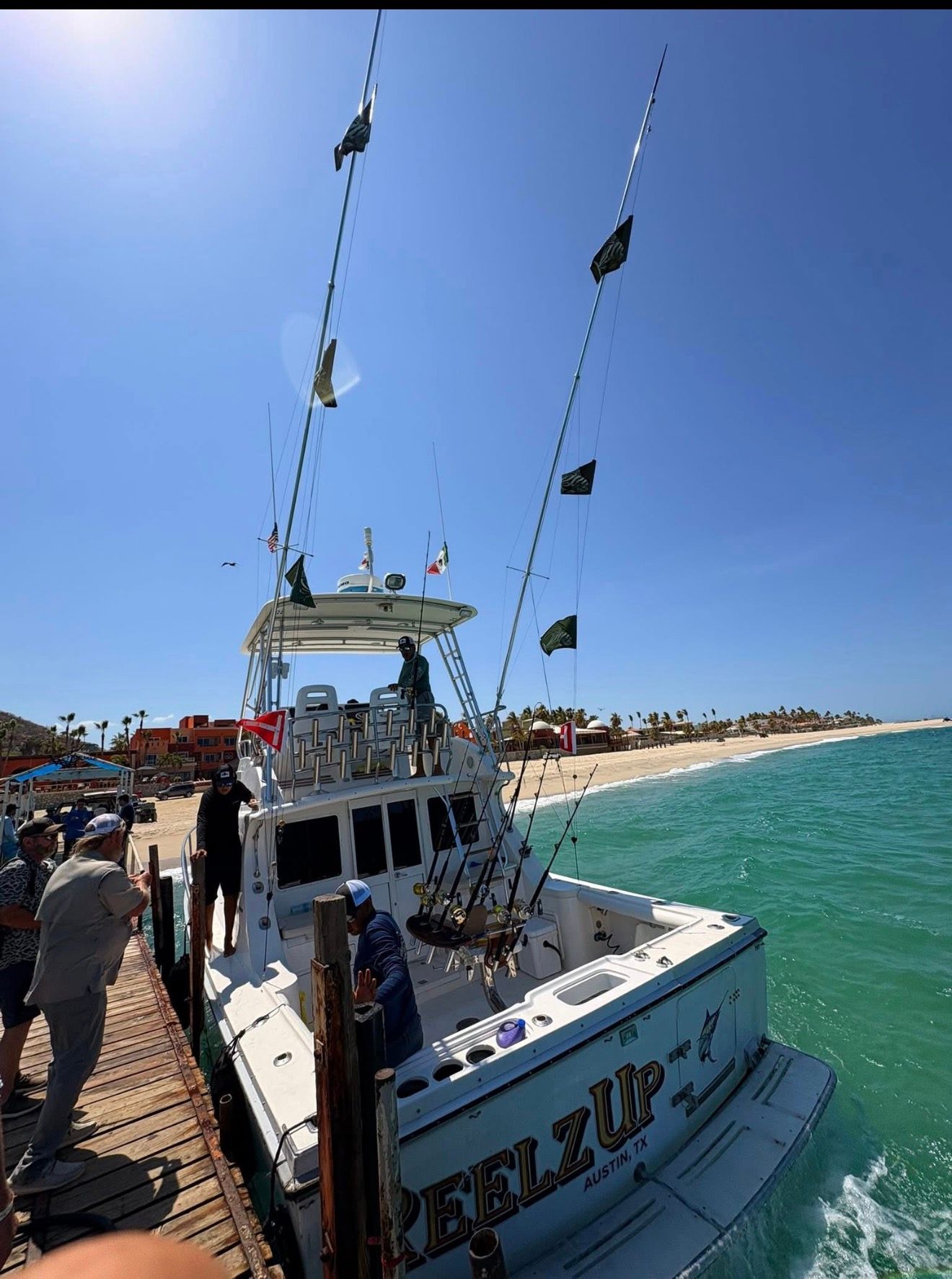 Fishing boat docked at a sunny marina beside a turquoise shoreline under a clear blue sky
