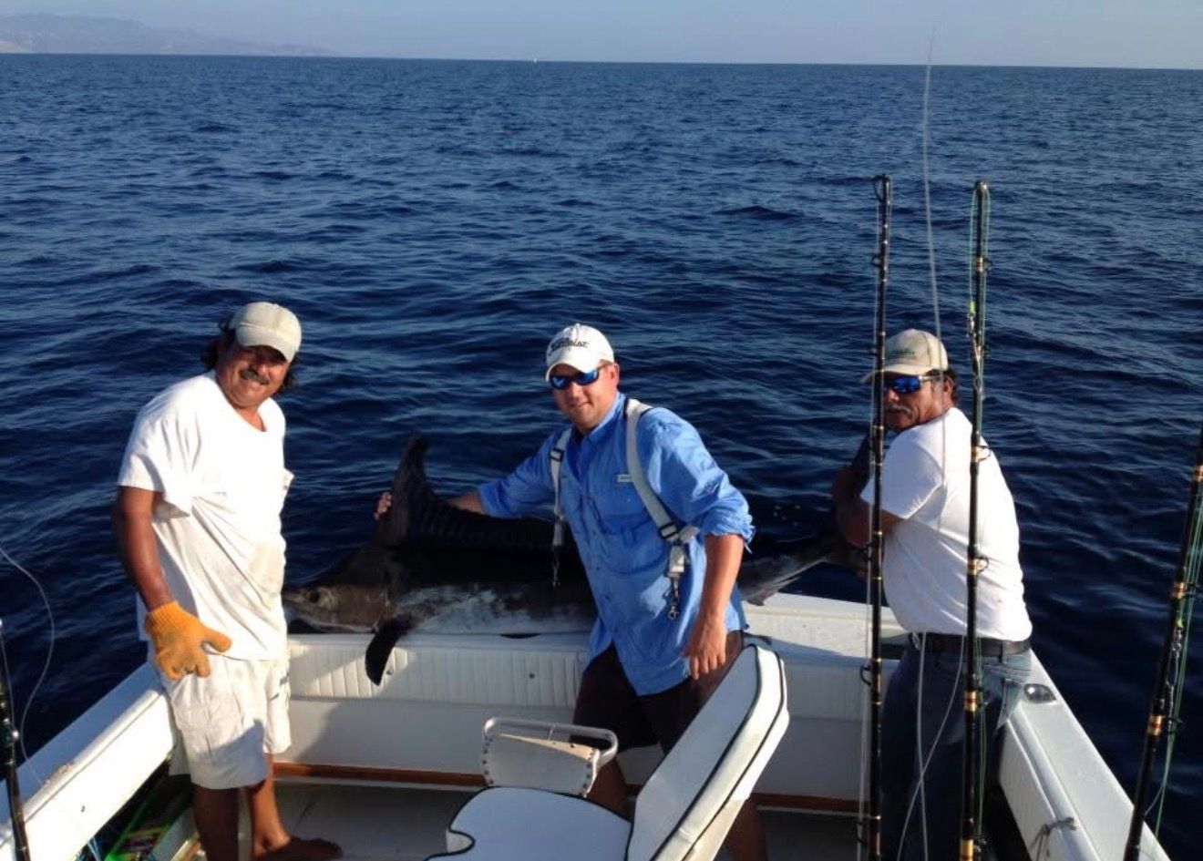 Three people on a boat at sea, holding fishing rods and posing with a catch.