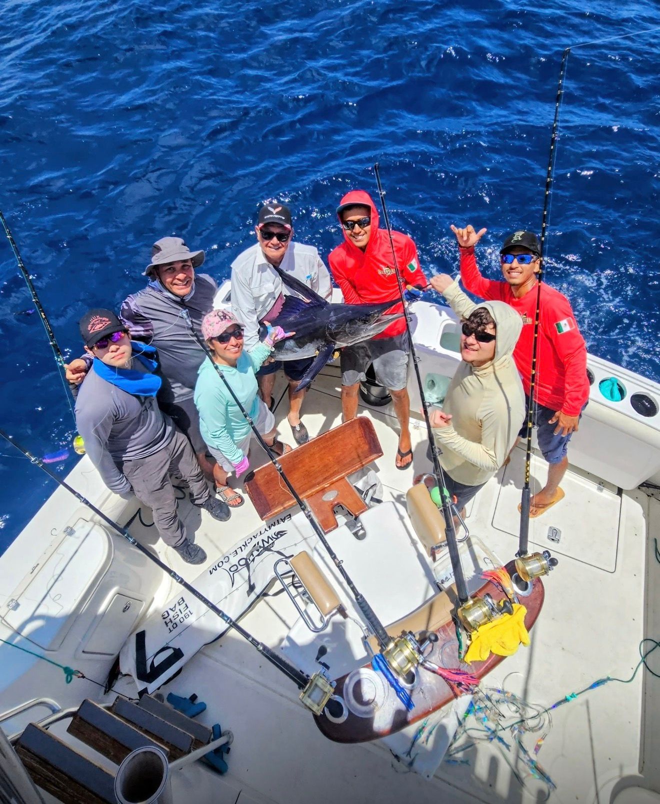 People on a fishing boat holding rods over deep blue water, smiling on deck